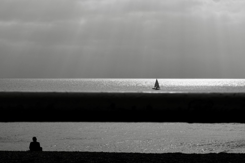black and white image of sea small yatch man reflecting sitting on the beach